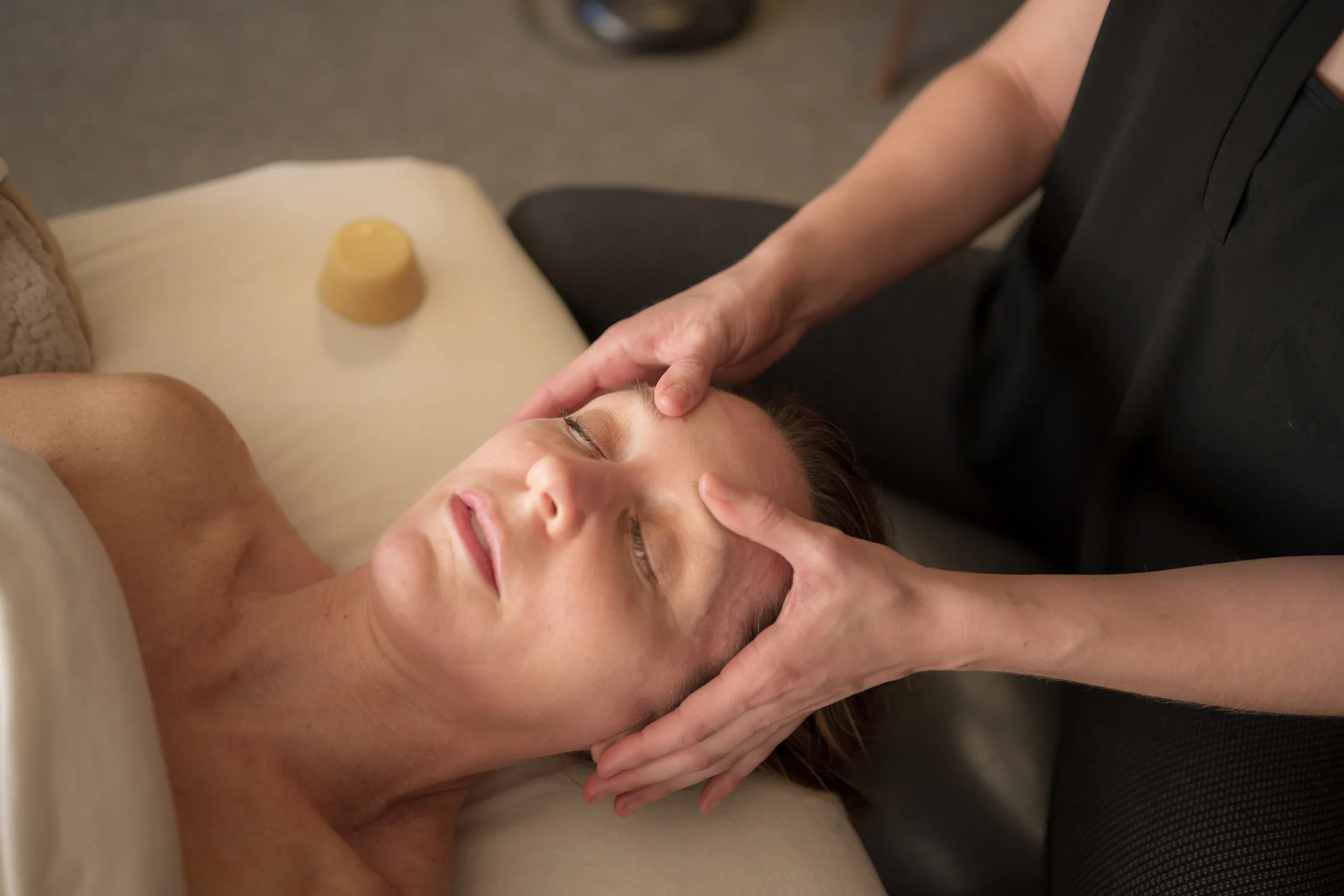 Katie cradling a client’s jaw and temple with both hands as they lie on the table with their eyes closed.